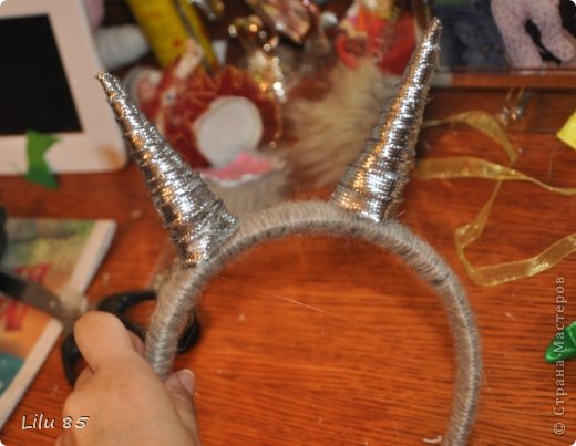 Для изготовления рожек для козы нам понадобятся: любая пластиковая бутылка, липкая лента, ножницы, серая и розовая лента, вата, обруч, желательно широкий, толстая серая шерстяная нить, клеевой пистолет, старый серый меховой воротник или другой мех. Украсьте углы цветами или лентами разных цветов. Для начала разрежьте пластиковую бутылку на два квадрата. Скрутите квадраты, чтобы получилась плюшевая игрушка, и прикрепите ее липкой лентой. С первого раза может не получиться, поэтому покрутите и отпустите квадратики несколько раз, чтобы 