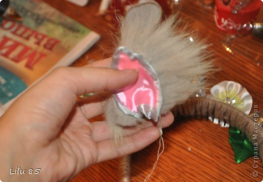 Вам понадобятся: любая пластиковая бутылка, липкая лента, ножницы, серая и розовая лента, вата, широкий ободок, толстая серая шерстяная нить, клеевой пистолет, старый серый меховой воротник или другой мех. Украсьте углы цветами или лентами разных цветов. Для начала разрежьте пластиковую бутылку на два квадрата. Скрутите квадраты, чтобы получилась плюшевая игрушка, и прикрепите ее липкой лентой. С первого раза может не получиться, поэтому покрутите и отпустите квадратики несколько раз, чтобы 